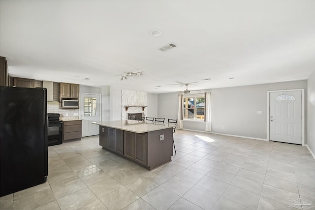 kitchen with a center island, tasteful backsplash, dark brown cabinets, light tile patterned floors, and black appliances