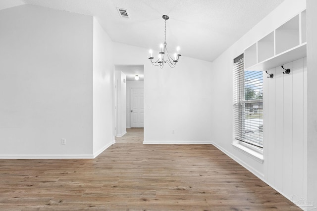 unfurnished dining area featuring hardwood / wood-style floors, an inviting chandelier, a textured ceiling, and vaulted ceiling