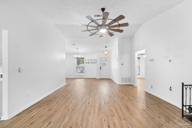 unfurnished living room featuring a textured ceiling, ceiling fan with notable chandelier, light hardwood / wood-style floors, and vaulted ceiling