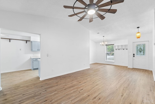 unfurnished living room featuring ceiling fan with notable chandelier, light wood-type flooring, a textured ceiling, and vaulted ceiling