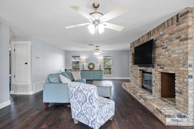 living room with a brick fireplace, dark wood-type flooring, and ceiling fan