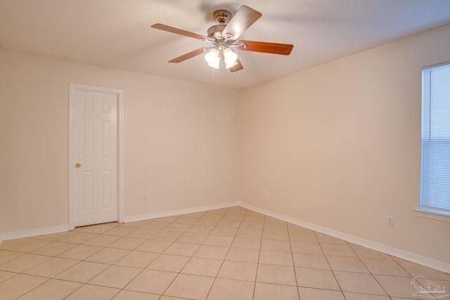 empty room with ceiling fan, light tile patterned floors, and baseboards