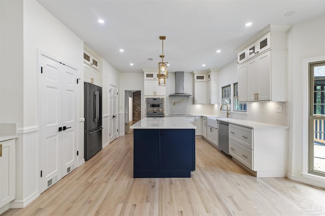 kitchen featuring wall chimney range hood, white cabinetry, black appliances, a kitchen island, and decorative light fixtures