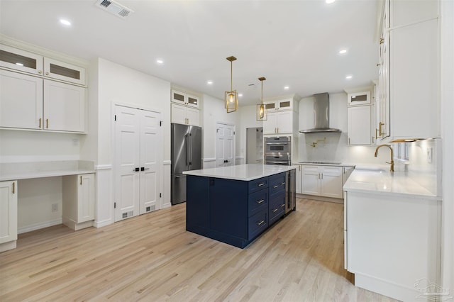 kitchen featuring a center island, wall chimney range hood, stainless steel appliances, light hardwood / wood-style floors, and white cabinets