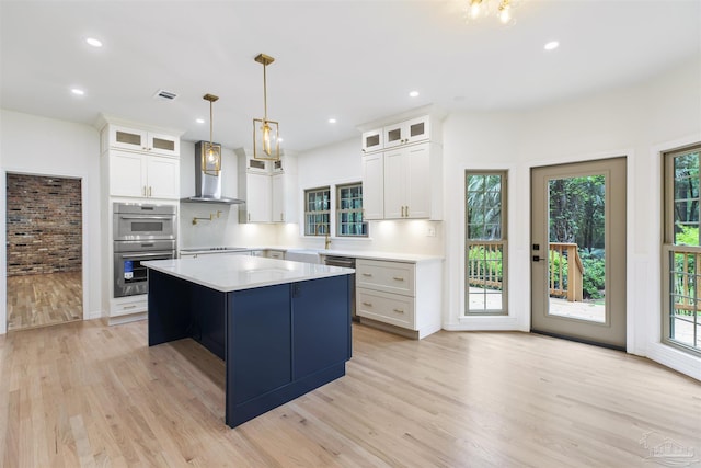 kitchen featuring wall chimney exhaust hood, light wood-type flooring, a kitchen island, and white cabinets