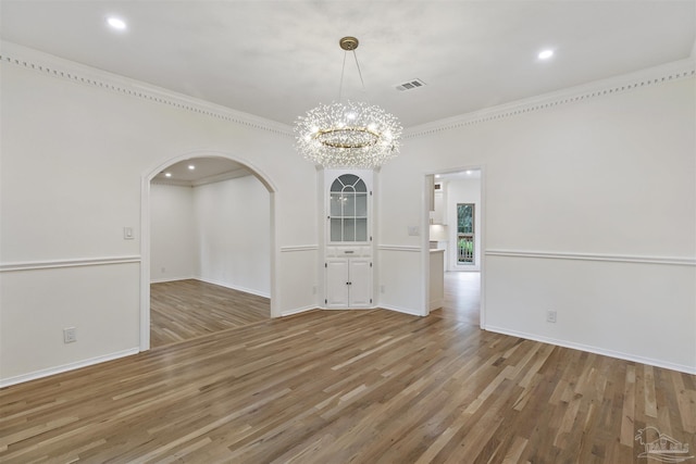 empty room with ornamental molding, hardwood / wood-style floors, and an inviting chandelier