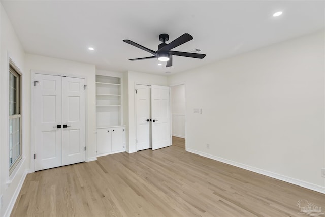 unfurnished bedroom featuring ceiling fan, light hardwood / wood-style floors, and multiple closets