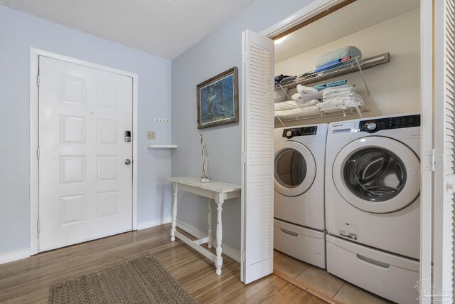 clothes washing area with light hardwood / wood-style flooring, washer and dryer, and a textured ceiling