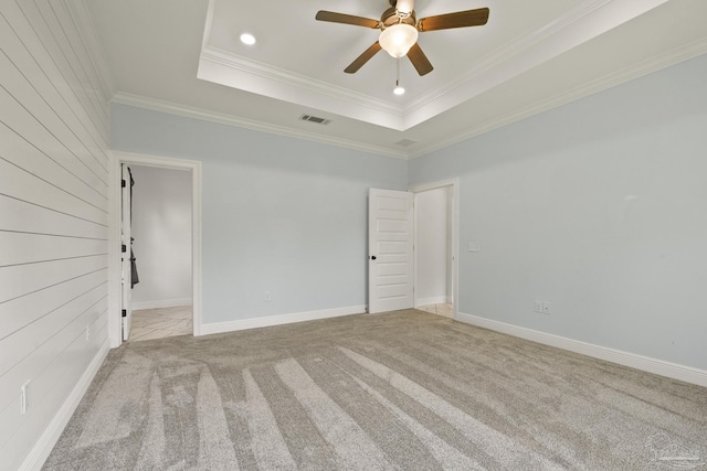 carpeted spare room featuring baseboards, ornamental molding, visible vents, a raised ceiling, and ceiling fan