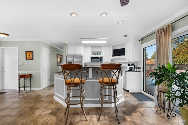 kitchen featuring a breakfast bar area, dark stone countertops, stainless steel appliances, ornamental molding, and white cabinets