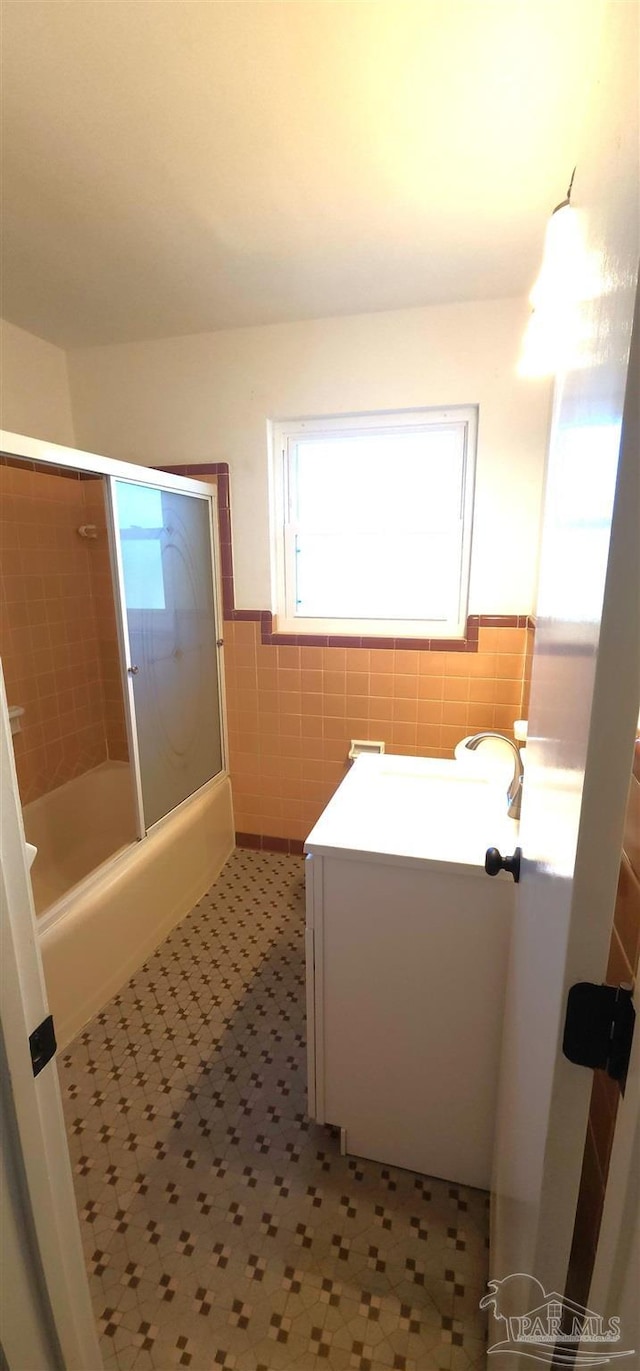 bathroom with combined bath / shower with glass door, vanity, and tile walls