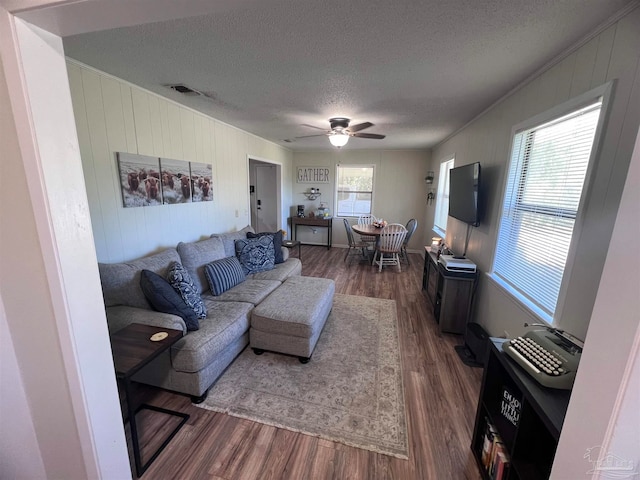 living room featuring a healthy amount of sunlight, a textured ceiling, ceiling fan, and dark wood-type flooring