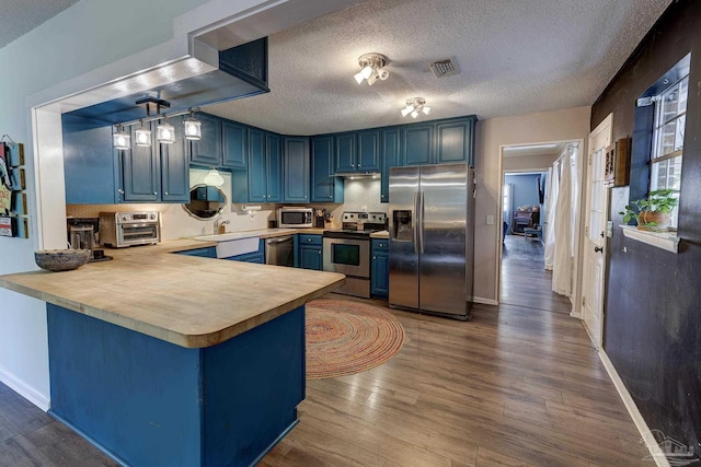 kitchen featuring blue cabinets, visible vents, appliances with stainless steel finishes, wood finished floors, and light countertops