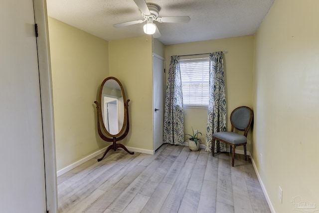 sitting room with a textured ceiling, baseboards, a ceiling fan, and light wood-style flooring