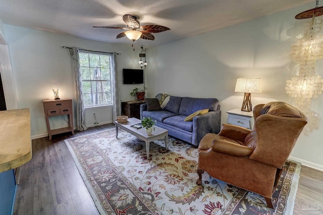 living area with a textured ceiling, baseboards, ceiling fan with notable chandelier, and wood finished floors