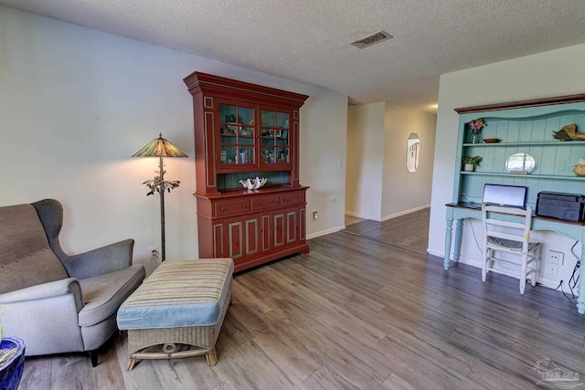 sitting room featuring baseboards, a textured ceiling, visible vents, and wood finished floors