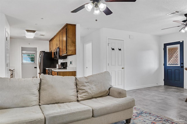 living room featuring a textured ceiling, ceiling fan, and light hardwood / wood-style flooring