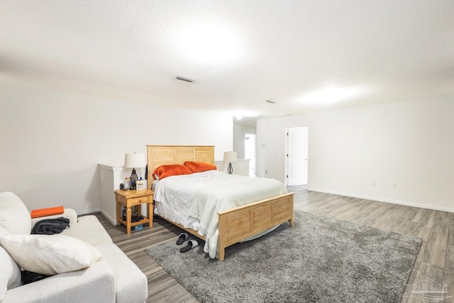 bedroom with a textured ceiling, light wood-style floors, visible vents, and baseboards