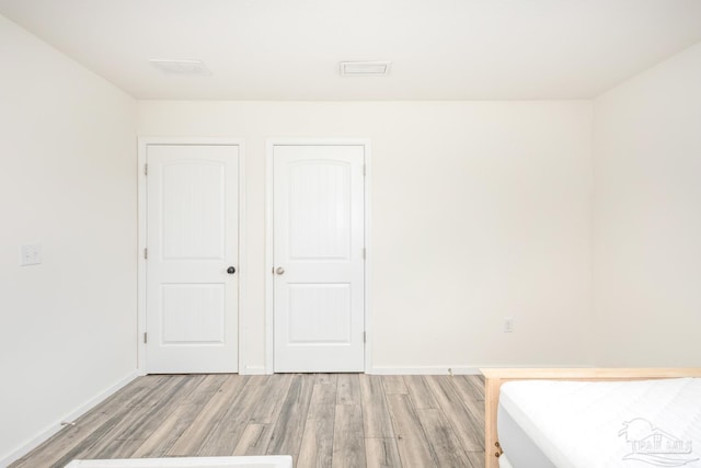 unfurnished bedroom featuring visible vents, light wood-type flooring, and baseboards