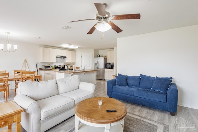 living area with light wood finished floors, visible vents, and ceiling fan with notable chandelier