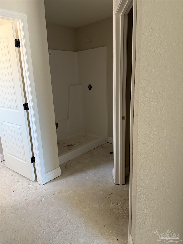full bath with a shower stall, baseboards, and a textured wall