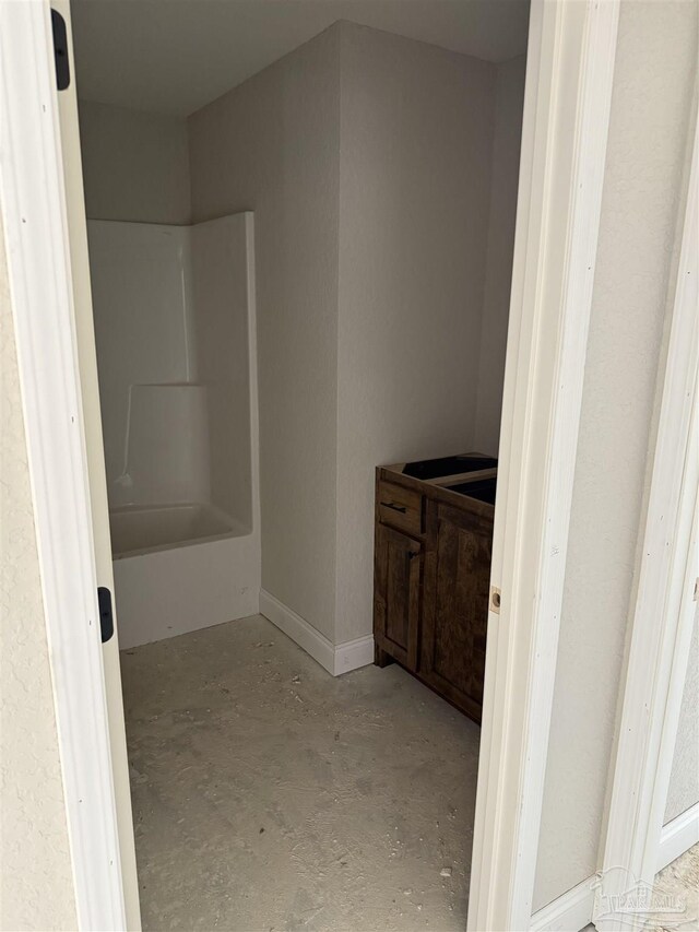 bathroom featuring unfinished concrete flooring, shower / bath combination, and baseboards
