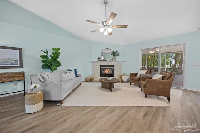 living room featuring a tile fireplace, vaulted ceiling, ceiling fan, and light hardwood / wood-style flooring