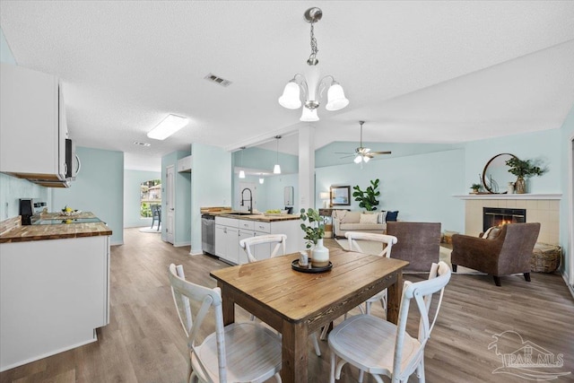 dining room with light hardwood / wood-style floors, vaulted ceiling, ceiling fan with notable chandelier, a fireplace, and a textured ceiling