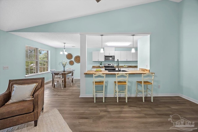 kitchen featuring appliances with stainless steel finishes, hanging light fixtures, a breakfast bar area, and dark hardwood / wood-style flooring