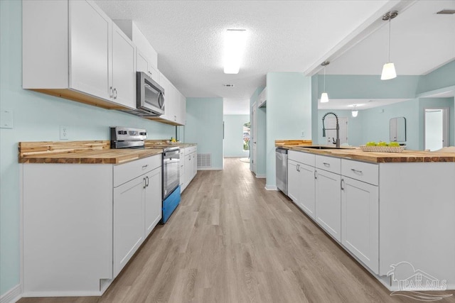 kitchen with stainless steel appliances, white cabinets, sink, and wooden counters