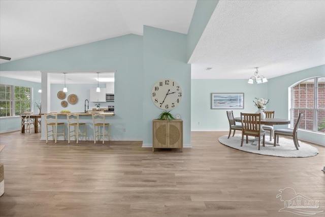 dining room featuring sink, light hardwood / wood-style flooring, vaulted ceiling, and a healthy amount of sunlight