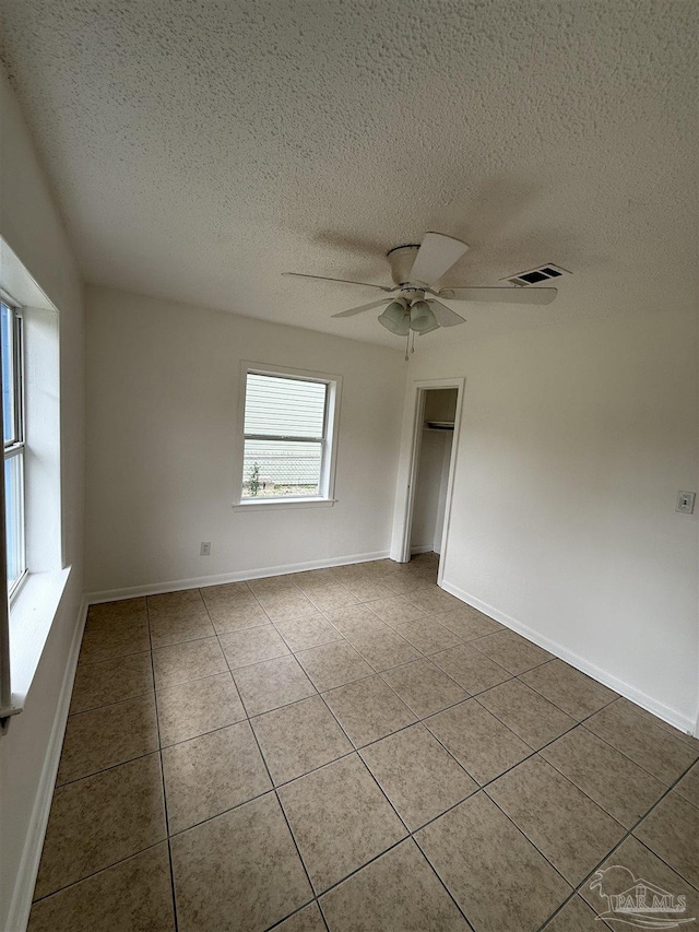 tiled empty room featuring visible vents, baseboards, and a ceiling fan