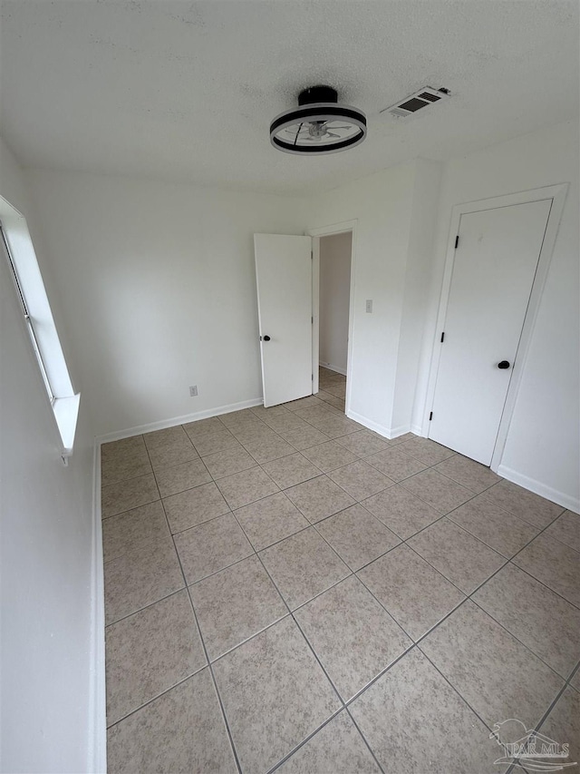 empty room featuring light tile patterned floors, baseboards, visible vents, and a textured ceiling