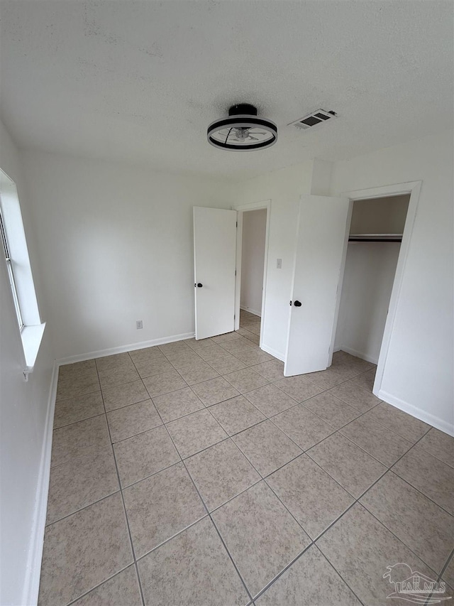 unfurnished bedroom featuring light tile patterned floors, baseboards, visible vents, and a textured ceiling