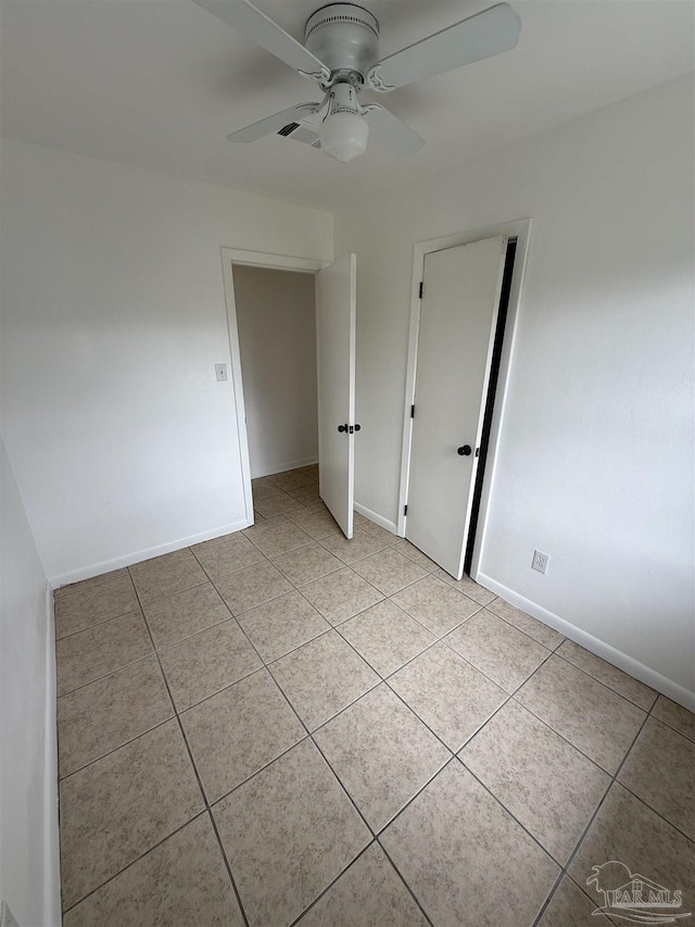 empty room with light tile patterned flooring, ceiling fan, and baseboards