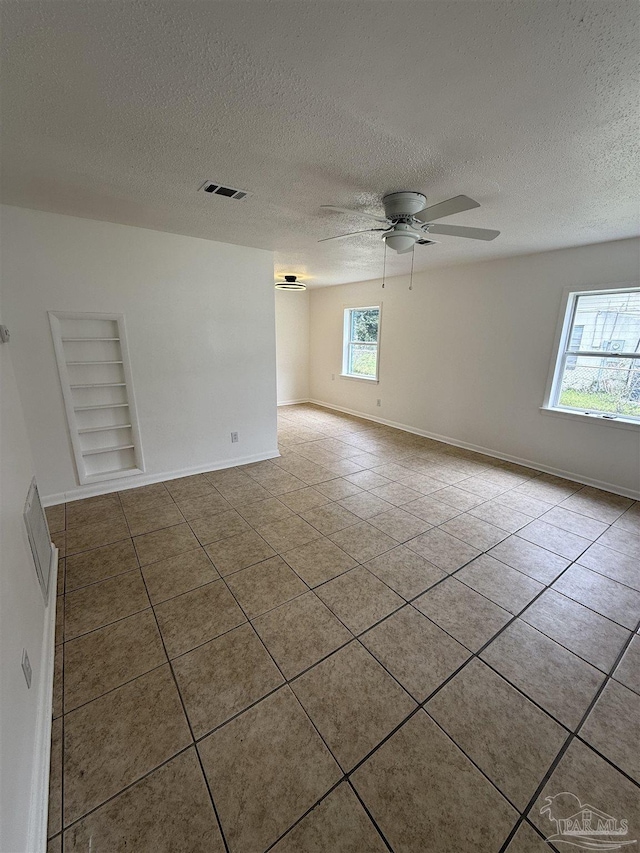 tiled empty room featuring built in shelves, a ceiling fan, visible vents, and baseboards