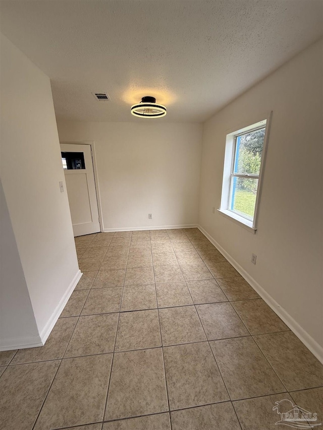 tiled spare room featuring baseboards, visible vents, and a textured ceiling