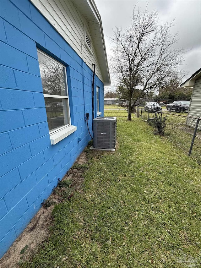 view of home's exterior with central air condition unit, concrete block siding, a yard, and fence