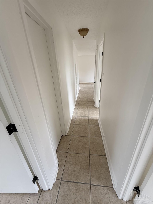 corridor featuring tile patterned flooring, a textured ceiling, and baseboards