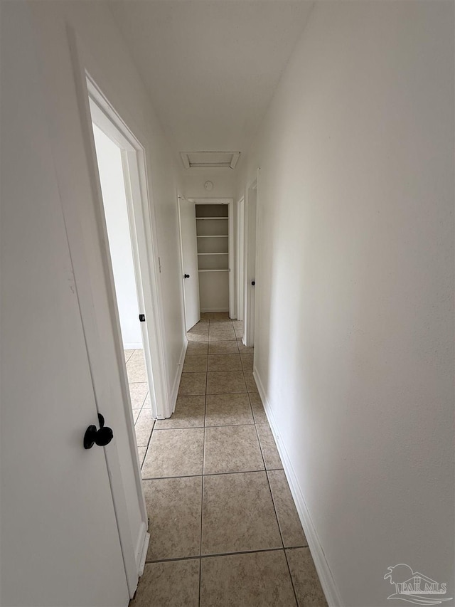 hallway with light tile patterned floors, attic access, and baseboards