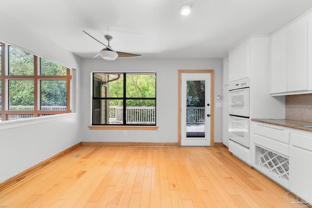 kitchen featuring baseboards, light wood-style flooring, ceiling fan, white cabinetry, and double oven