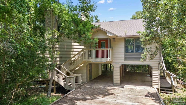 raised beach house with a carport, stairway, concrete driveway, and roof with shingles