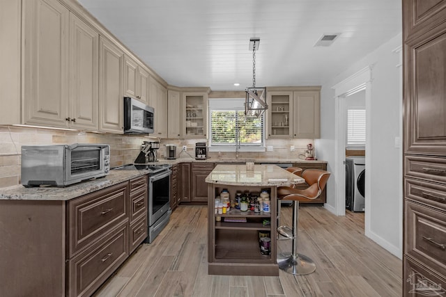 kitchen featuring cream cabinetry, a toaster, washer / clothes dryer, stainless steel appliances, and open shelves