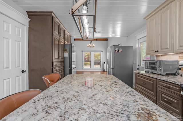 kitchen featuring freestanding refrigerator, light stone countertops, a chandelier, and a toaster