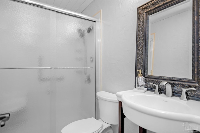 full bathroom featuring a sink, a textured wall, toilet, and a stall shower