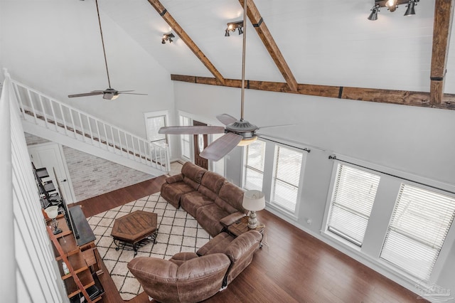 living room featuring beam ceiling, wood finished floors, ceiling fan, and stairway