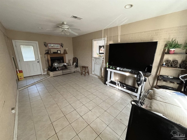 tiled living room with ceiling fan and brick wall