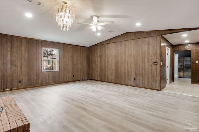 spare room with wood walls, lofted ceiling, ceiling fan with notable chandelier, and light wood-type flooring