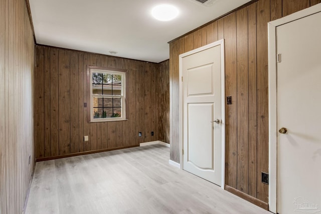 unfurnished room featuring wooden walls and light hardwood / wood-style floors