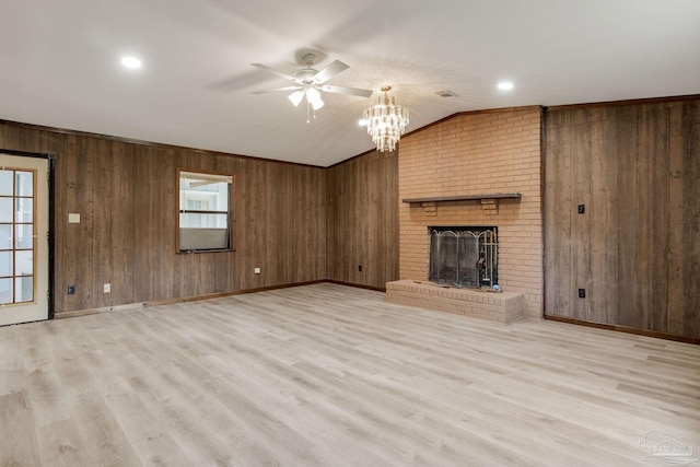 unfurnished living room featuring light hardwood / wood-style floors, ceiling fan with notable chandelier, a brick fireplace, and wooden walls